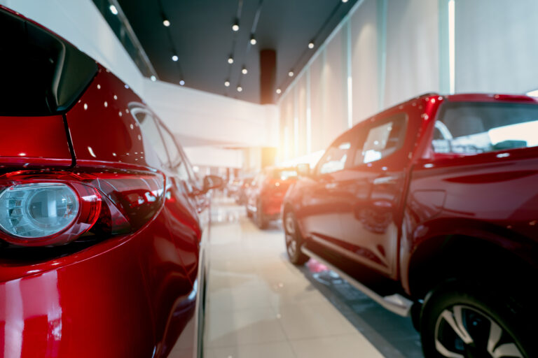 Rear view of red car parked in luxury showroom. Car dealership office. New car parked in modern showroom. Car for sale and rent business concept. Automobile leasing and insurance. Closeup tail light.